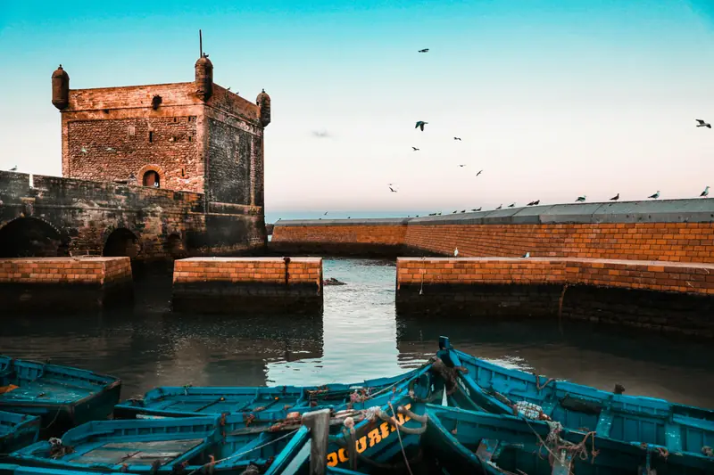 Bastione e barche blu dei pescatori nel porto di Essaouira